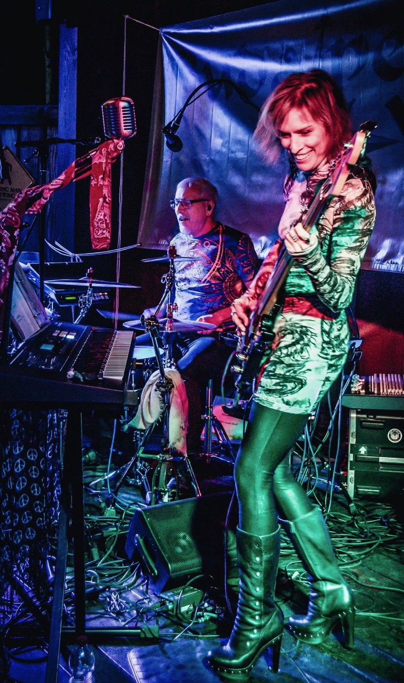 Kathy Johnson playing bass with Budapest West under colorful stage lights.