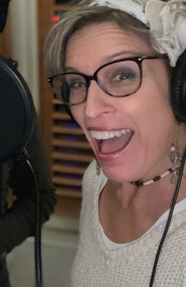 Kathy Johnson smiling in headphones beside a studio microphone.